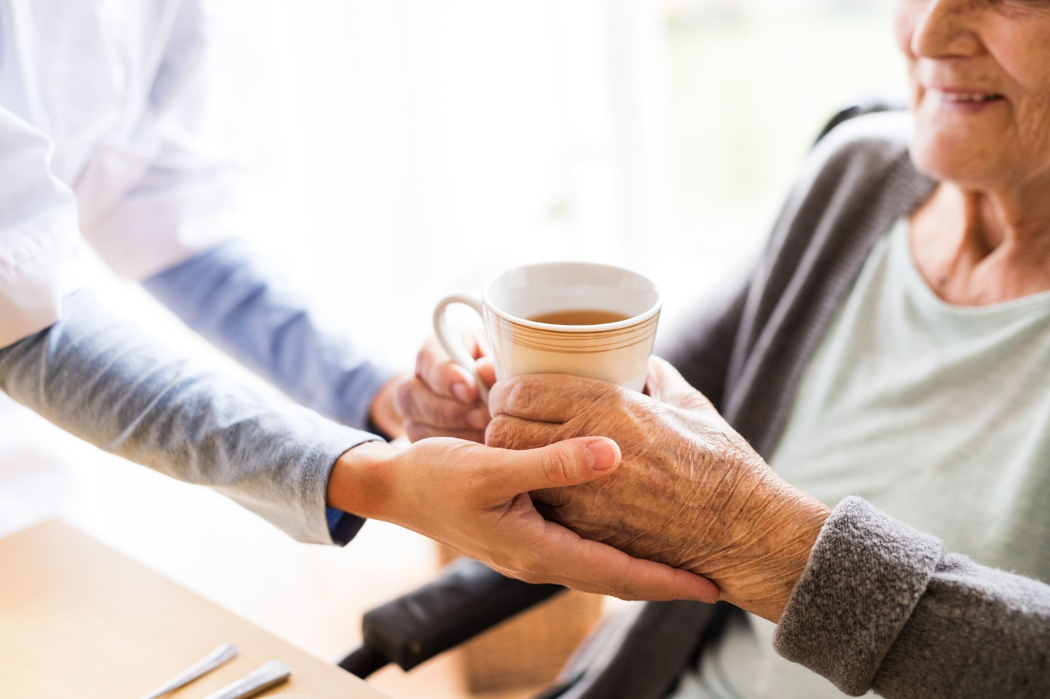 Ältere Person hält eine Tasse, die von einer anderen Person unterstützt wird